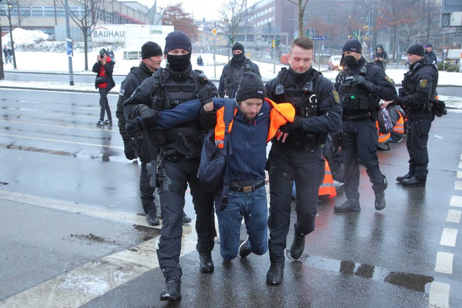 Nachdem die Hand eines zuvor festgeklebten Unterstützers der "Letzten Generation" von der Polizei mit einem Speiseöl von der Straße gelöst wurde, wird er aus Sicherheitsgründen von der Fahrbahn getragen.