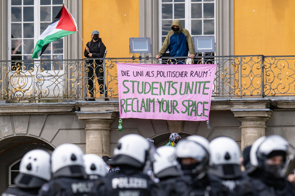 Zwei vermummte Demonstranten auf einem Balkon schwenken eine palästinensische Fahne.