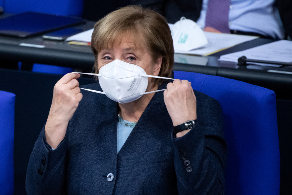 Bundeskanzlerin Angela Merkel setzt sich zu Beginn der Plenarsitzung im Deutschen Bundestag ihre FFP-Maske ab.