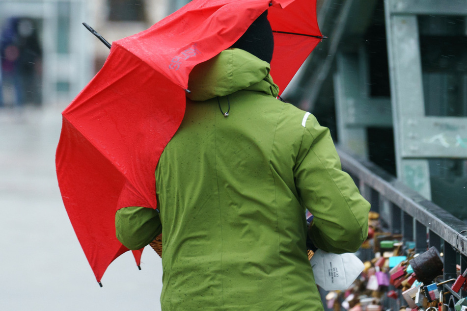 Ein Mann mit Schirm auf dem "Eisernen Steg" in Frankfurt am Main - am Montag muss in Hessen noch örtlich mit leichtem Regen gerechnet werden.