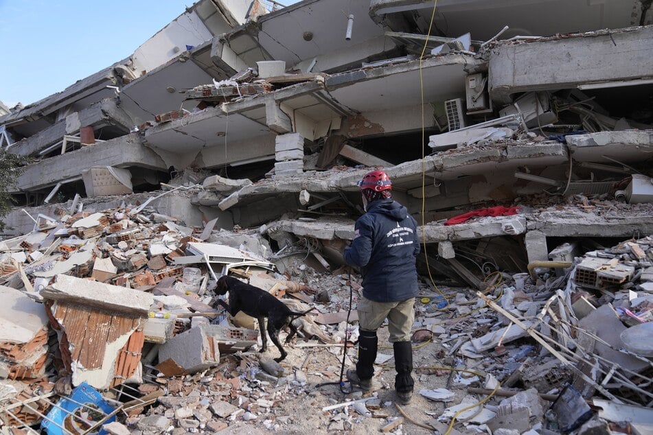 Ein Retter mit einem Spürhund sucht in einem zerstörten Gebäude in Antakya nach Überlebenden des Erdbebens.