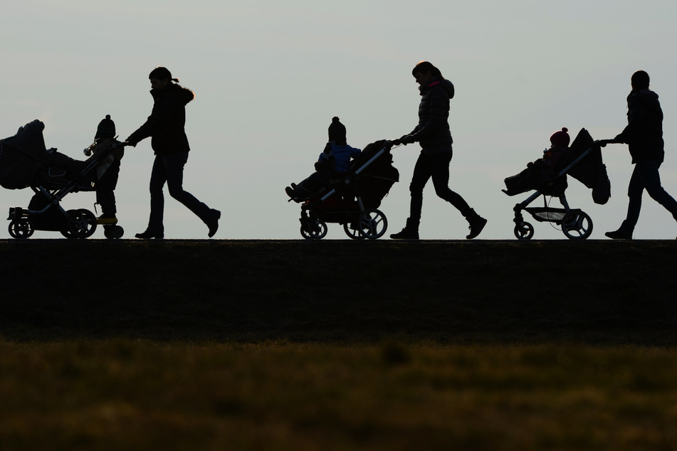 Drei Mütter schieben ihre Kinderwagen eine Landstraße entlang.